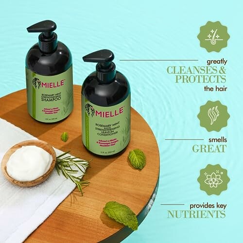 Mielle Rosemary Mint Shampoo and Conditioner bottles on a wooden surface with mint leaves and a bowl of cream.