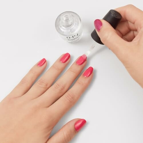 Applying clear nail polish over pink nails.