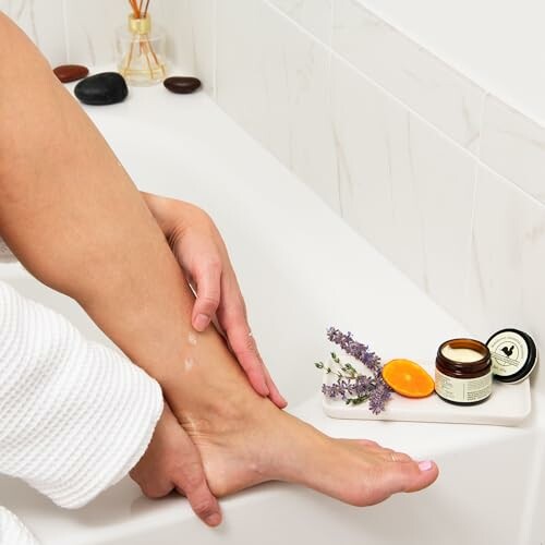 Person applying cream to leg near bathtub with skincare products.